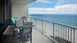 A balcony with a table and chairs, a vase with flowers, and a view of the sea and a pier. - Phoenix Gulf Shores Ii 1002 3 Bedroom Condo (Gulf Shores)