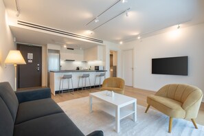 A modern living room with a sofa, armchair, coffee table, and a kitchen area with bar stools. - LIV Athinum 1 - Luxury Apartment 1B (Athens)
