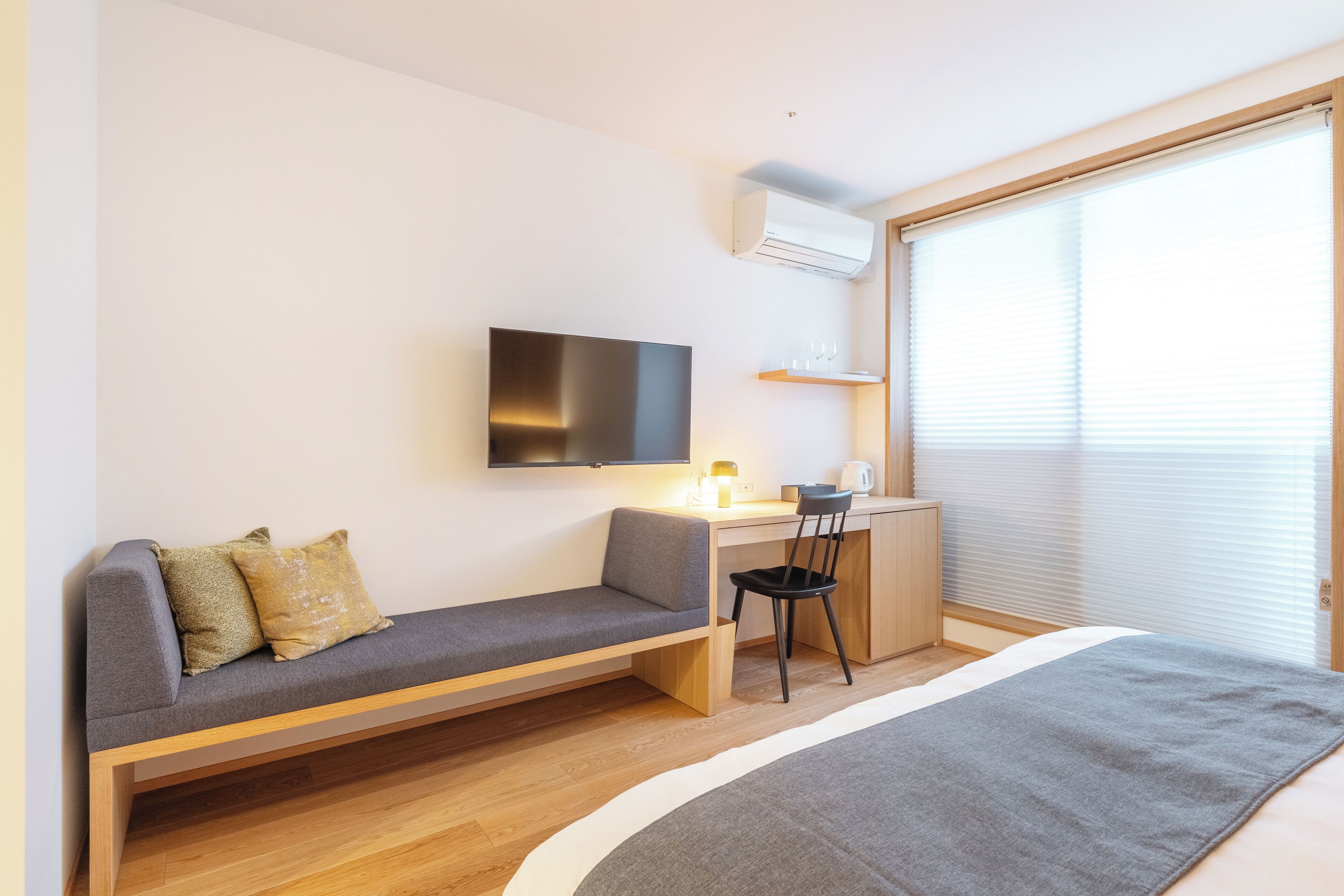 Une chambre moderne équipée d’un canapé, d’un bureau, d’une chaise, d’une télévision et d’une fenêtre avec des stores.