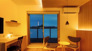 Een moderne kamer met een houten bureau, twee stoelen, een kleine tafel en een groot raam met uitzicht op een stadsbeeld 's nachts.
