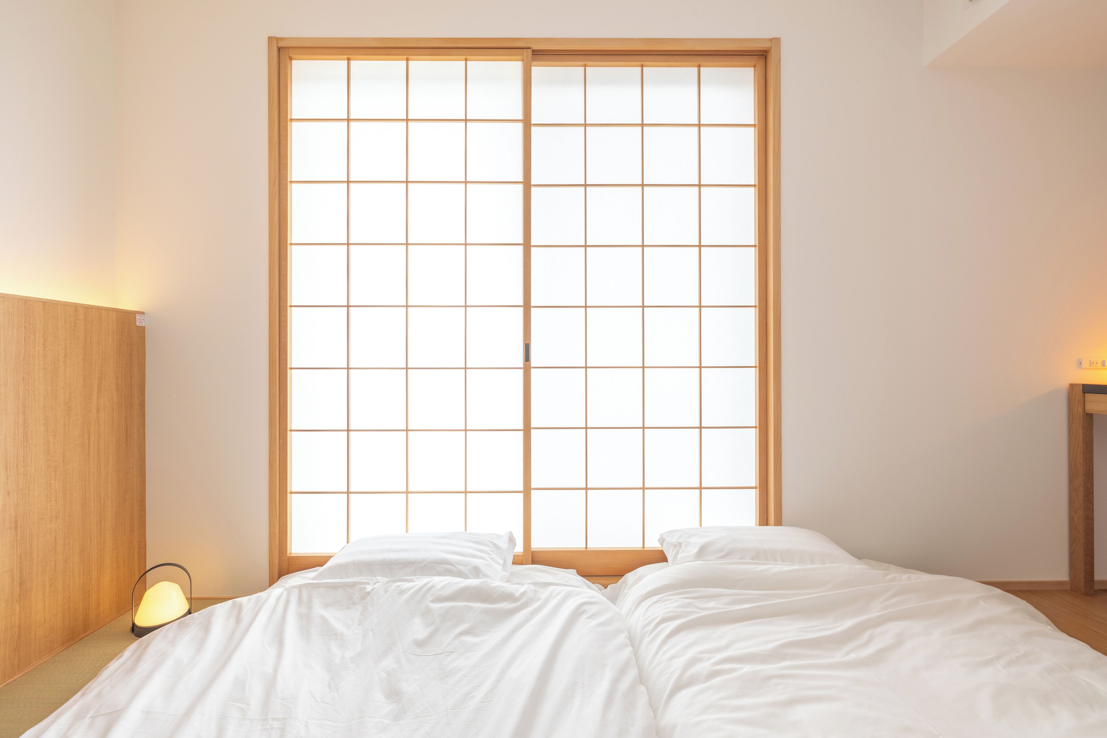 Una habitación con una cama, cabecera de madera, una mesita de noche con lámpara y una puerta corredera con pantalla shoji.