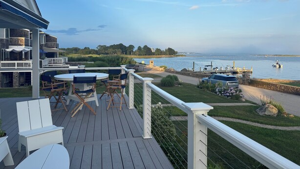 A deck with outdoor furniture overlooking a body of water, boats, and a distant shoreline. - 4BR Oceanview Academic Rental in Stonington CT 09/01 thru 05/31 (Stonington)