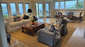 A spacious living room with a large window overlooking a body of water, a sofa, a coffee table, and a seating area with chairs. - 4BR Oceanview Academic Rental in Stonington CT 09/01 thru 05/31 (Stonington)