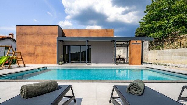Un área moderna junto a la piscina, con una piscina azul cristalina, dos sillas de descanso con toallas y un conjunto de columpios de madera.