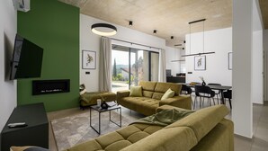 Una sala de estar moderna con una pared verde decorativa, un juego de sofá, un televisor de pantalla plana y un comedor con mesa y sillas.