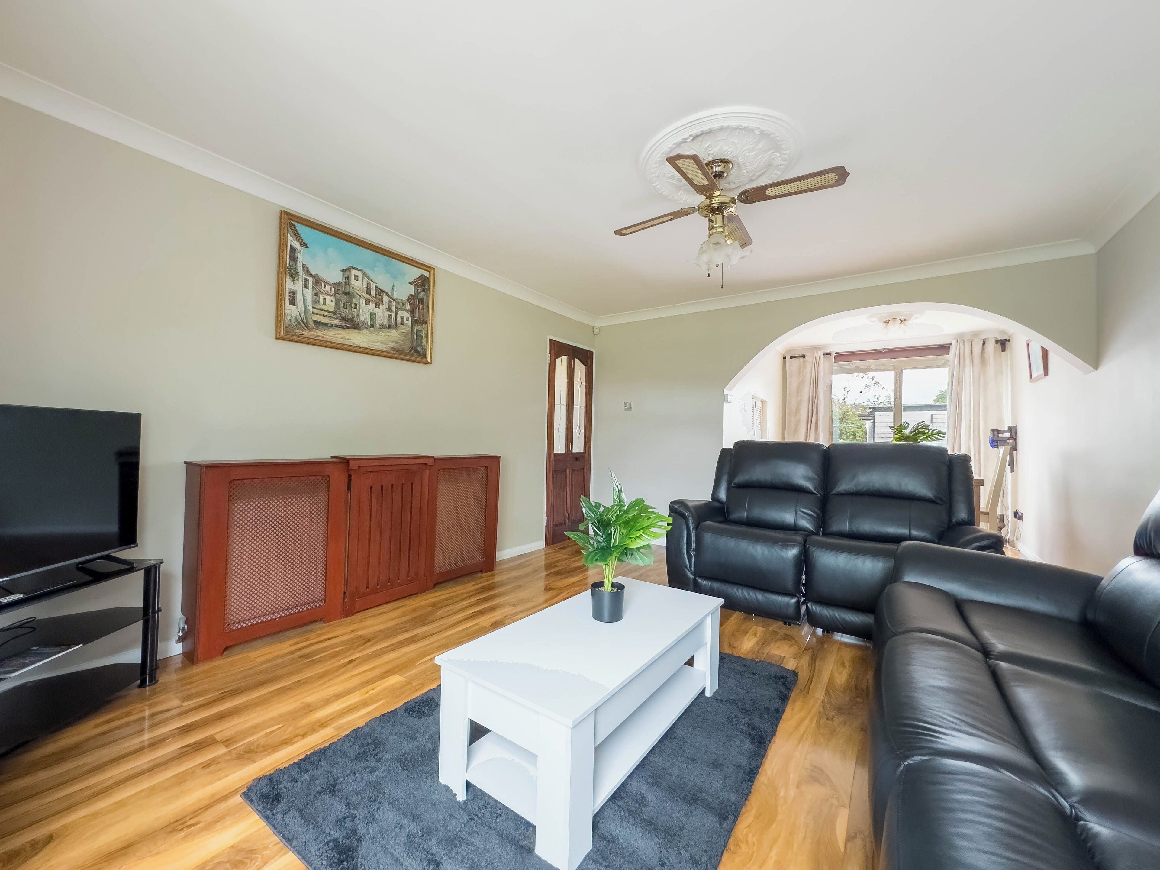 A living room with a television, a white coffee table, a black leather sofa, and a ceiling fan.