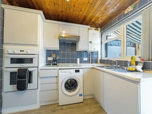 A compact kitchen with a washing machine, a built-in oven, and a window with a view.