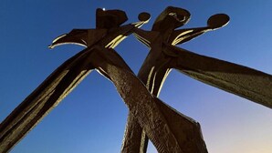Eine Skulptur abstrakter Figuren vor blauem Himmel.