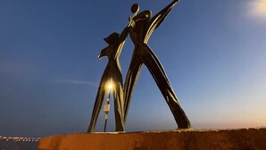 Eine Skulptur von zwei Figuren mit ausgestreckten Armen vor einem Dämmerhimmel.