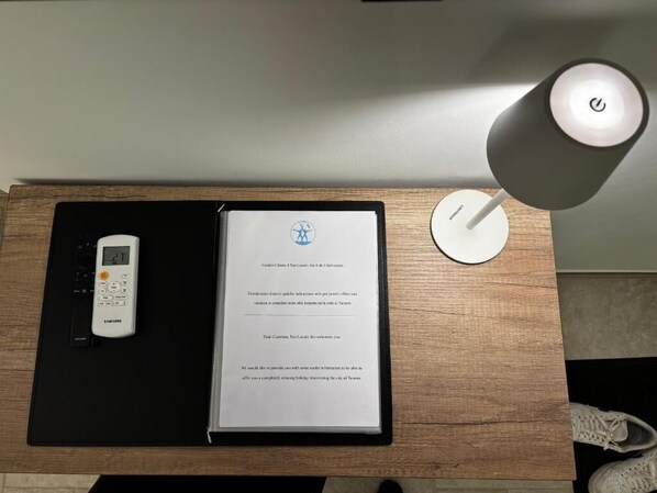 A desk with a Samsung phone, a framed welcome letter, and a lamp.
