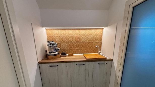 Eine kleine Küche mit einer Holzarbeitsplatte, eingebauten Schränken und einer gemusterten Spritzschutzwand.