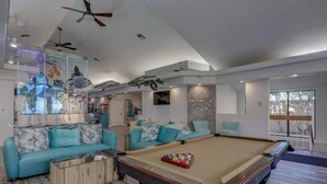 A modern living room with a pool table, sofas, and ceiling fans.