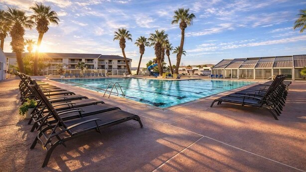A pool area with lounge chairs, palm trees, and a building with a swimming pool.