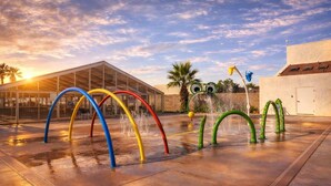An outdoor water play area with colorful arches and a glass building in the background.