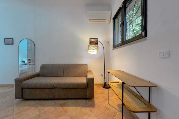 A living room with a sofa, a table, a lamp, and a window.