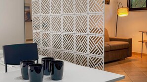 Een moderne kamer met een witte scheidingswand, een bank, een tafel met vier zwarte mokken en een vloerlamp.