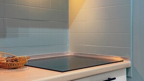 Een keuken met een glazen kookplaat, een wit kastje en een rieten mandje op het aanrecht.