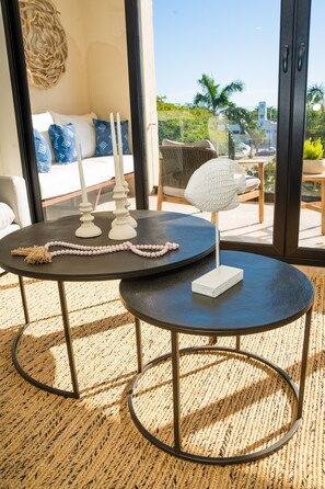 A modern room with a large window, a round table with candles, a white chair, and a sofa with patterned cushions.