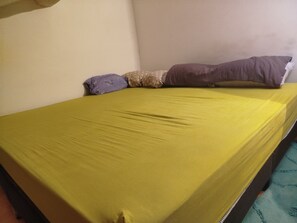 Uma cama de solteiro com edredom amarelo, duas almofadas e um cobertor azul.
