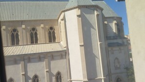 A building with a prominent tower and arched windows, viewed from a window with a tiled roof.