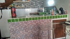 A kitchen with a stone backsplash, green and pink tiled counter, a microwave, and a coffee maker.