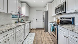 Une cuisine moderne avec des meubles blancs, un réfrigérateur en acier inoxydable, un four à micro-ondes, un four traditionnel et un plan de travail en granit.