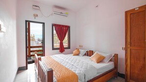 Une chambre avec un lit en bois, une fenêtre avec des rideaux rouges, un appareil de climatisation et une vue sur les bâtiments à l’extérieur.