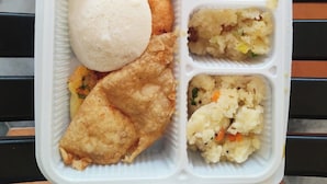 Un repas servi dans un plateau compartimenté, comprenant différents plats, notamment un aliment rond et blanc, des aliments frits et des plats à base de légumes variés.