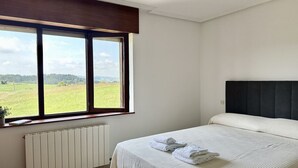 A bedroom with a bed, a window with a view of a field, and a radiator. - La Atalaya del Cabo - 4800 (Arnuero)