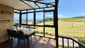 A dining area with a table and chairs, large windows, and a view of a green landscape. - La Atalaya del Cabo - 4800 (Arnuero)