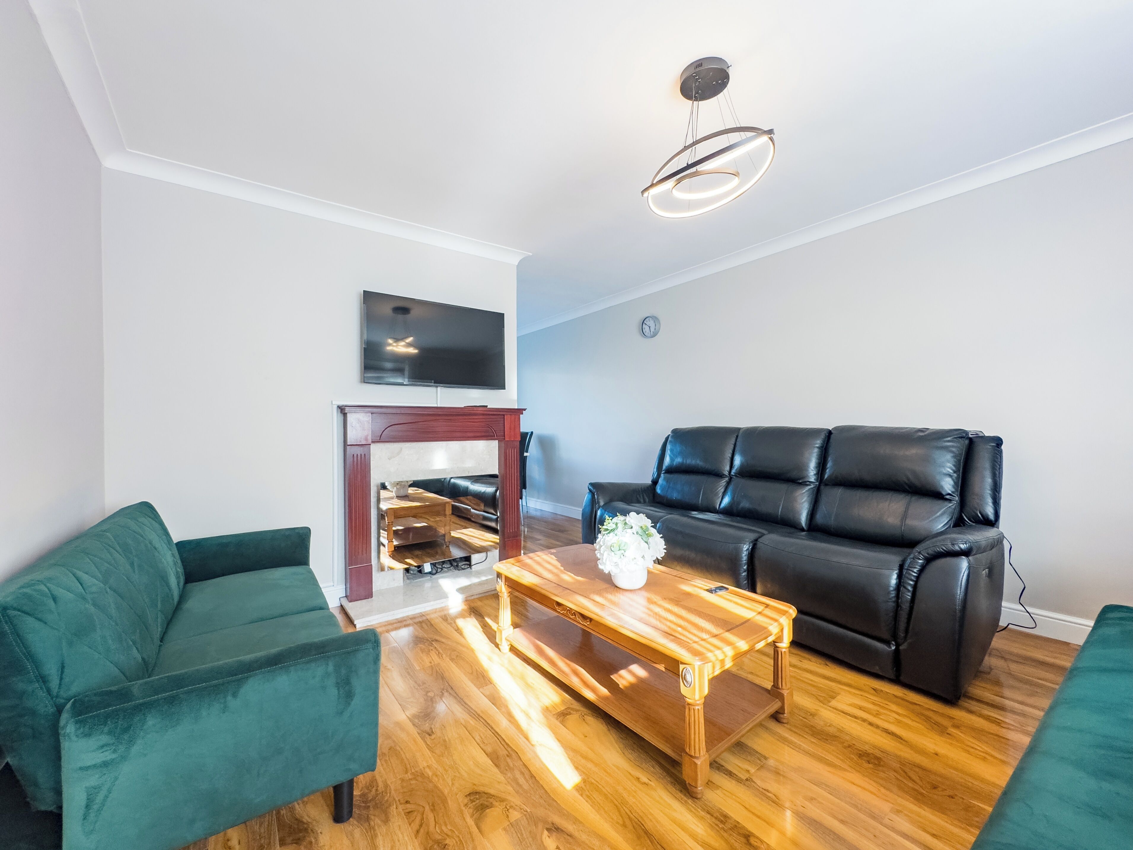 A modern living room with a black leather sofa, a green armchair, and a wooden coffee table. A flat-screen TV is mounted on the wall above a fireplace.
