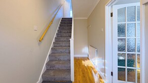 Un escalier dont les marches sont recouvertes de moquette, menant à un palier, avec un plancher en bois et une porte blanche dotée de panneaux en verre dépoli.