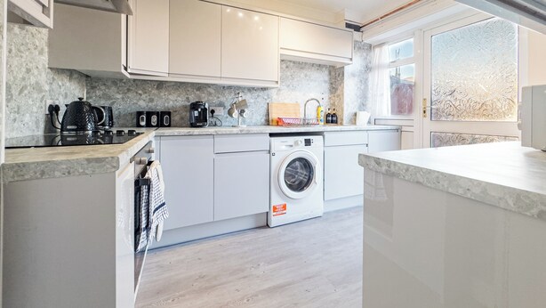 Une cuisine moderne avec des meubles blancs, un lave-linge encastré et un plan de travail équipé de divers appareils.