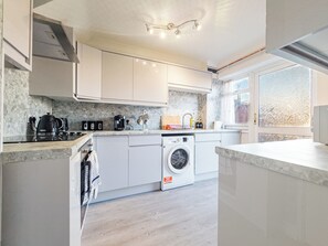 A modern kitchen with white cabinets, a built-in washing machine, and a countertop with various appliances. - House - Sleeps 7, Private Garden & Parking (Basildon)