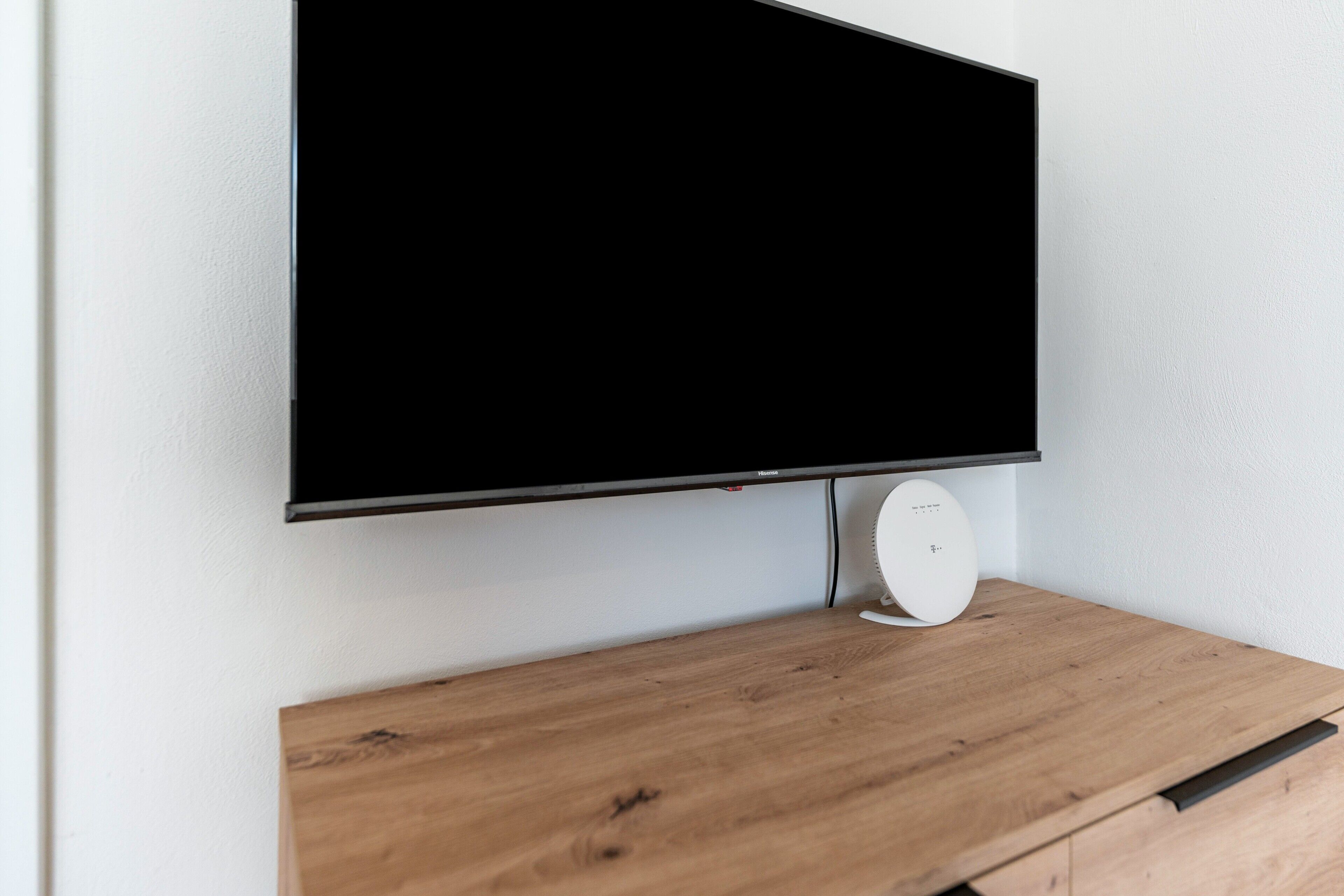A flat-screen TV mounted on a wooden stand with a white wall in the background.