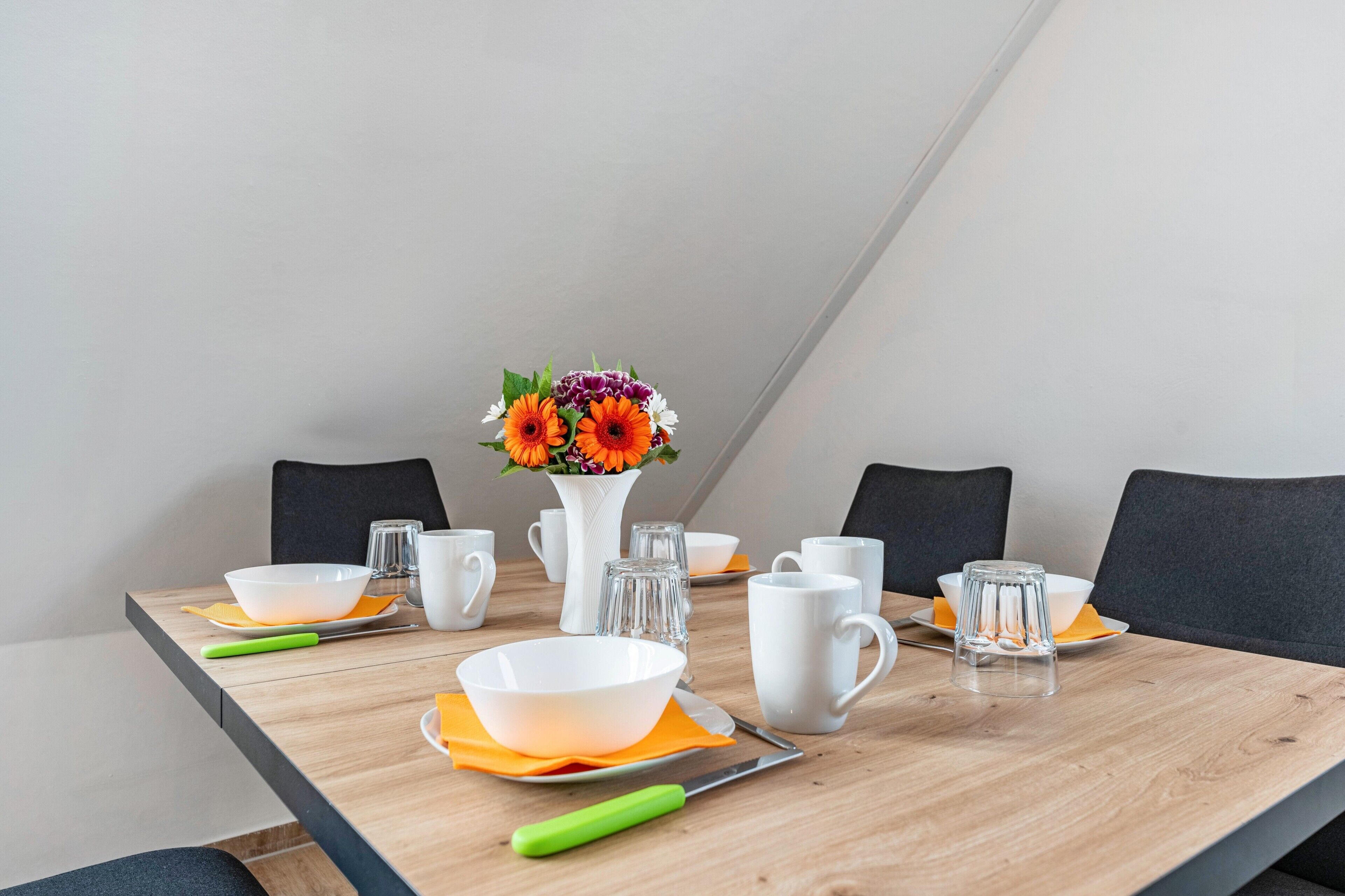 Une table à manger avec des bols et des tasses blancs, ainsi qu’un vase rempli de fleurs.