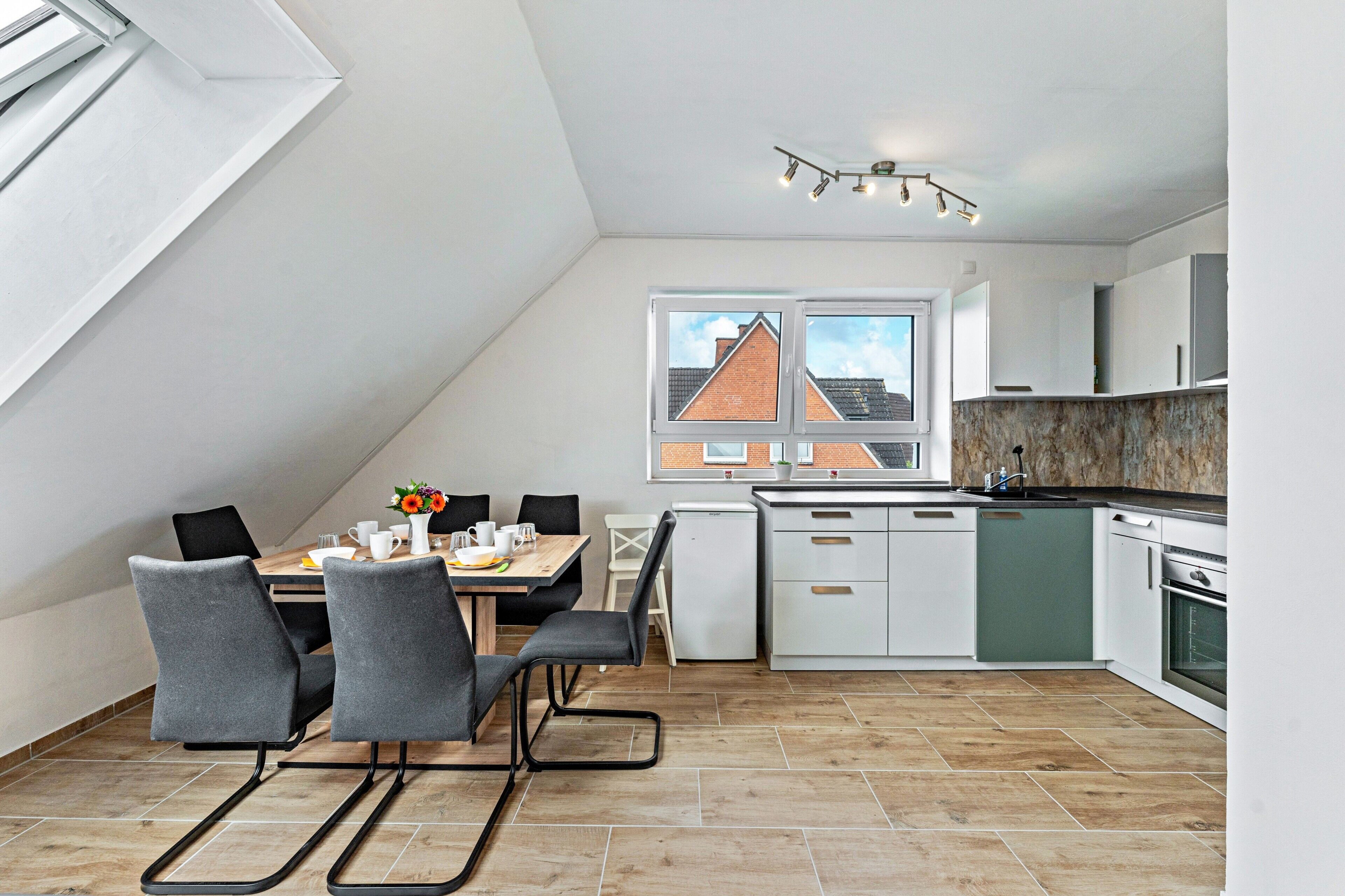 Een moderne keuken met een eethoek, witte kasten en uitzicht op een gebouw van baksteen.