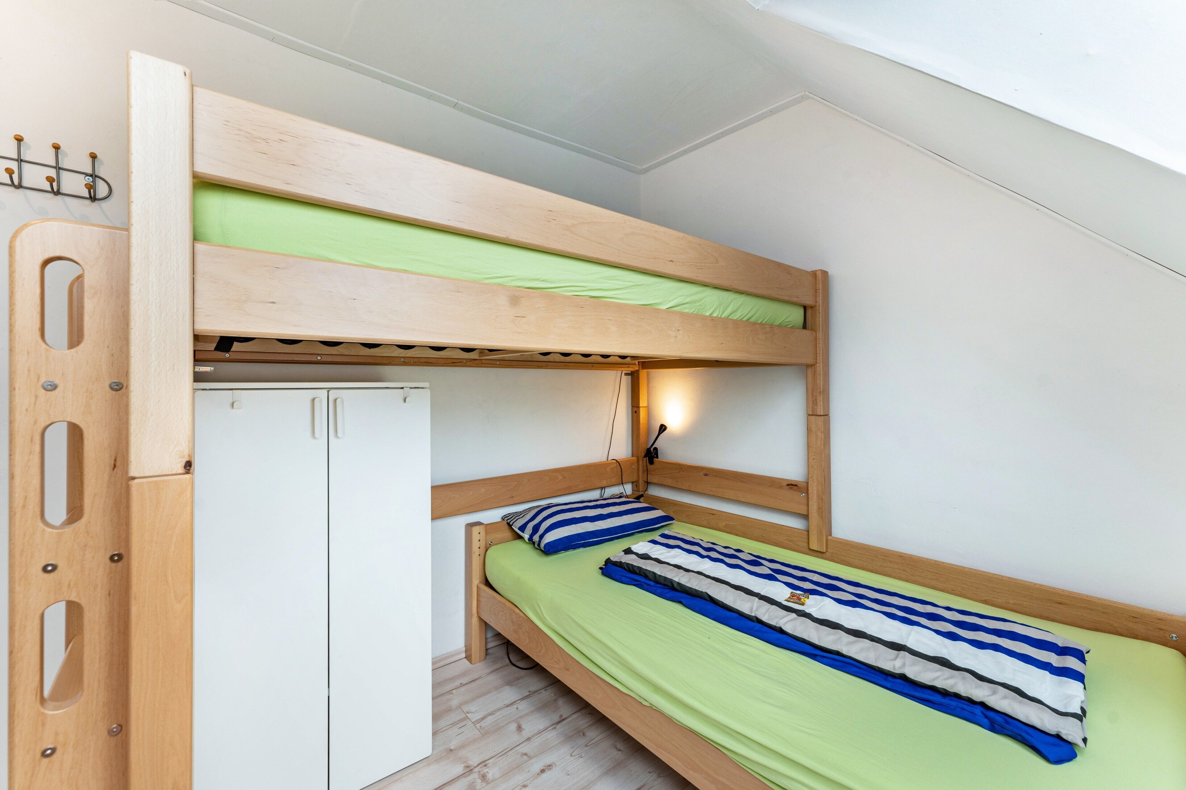 Ein Etagenbett mit einer grünen Matratze, einem Holz-Kopfstück und einer weißen Tür.
