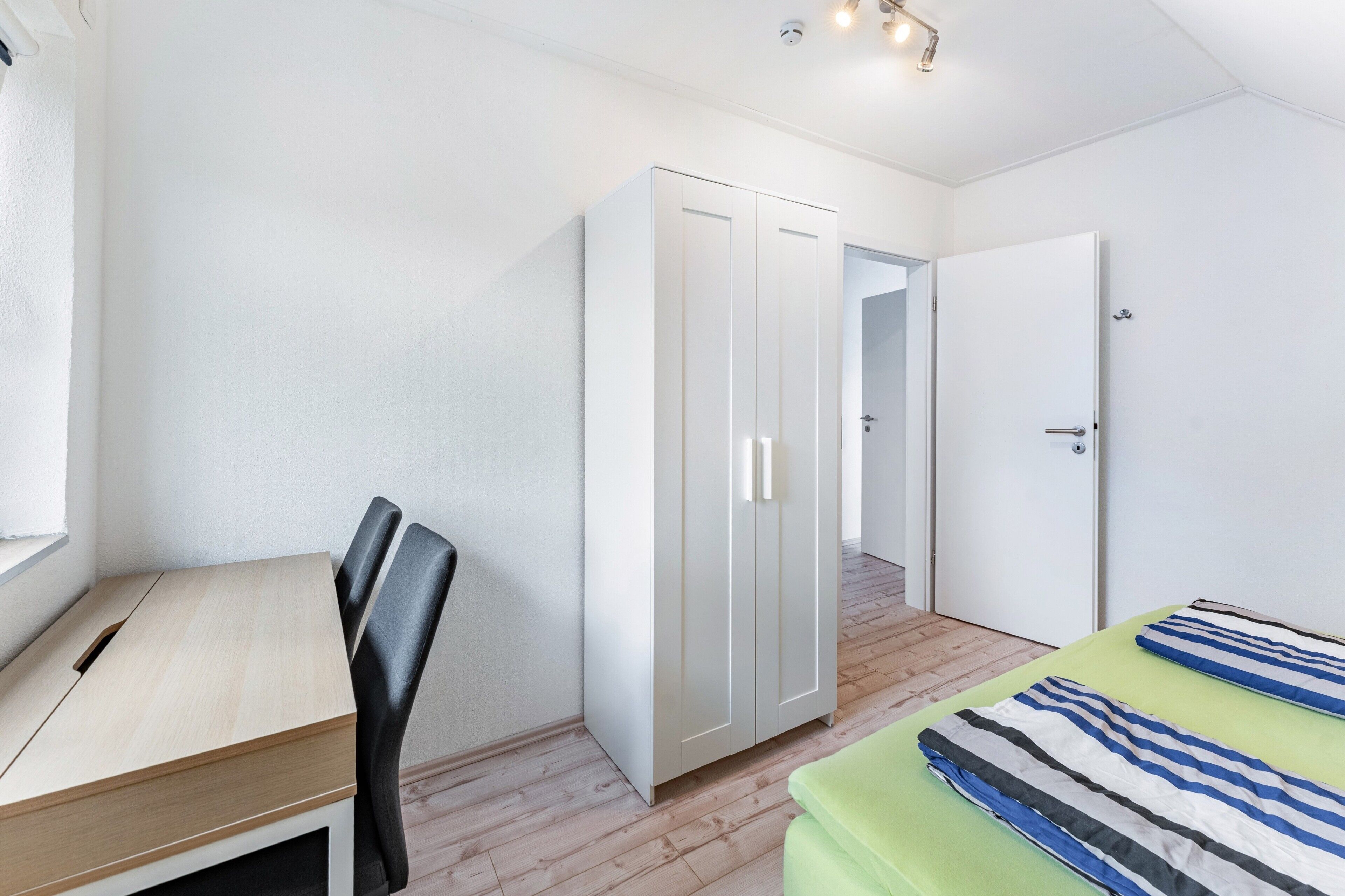 A bedroom with a bed, a desk, and a wardrobe.