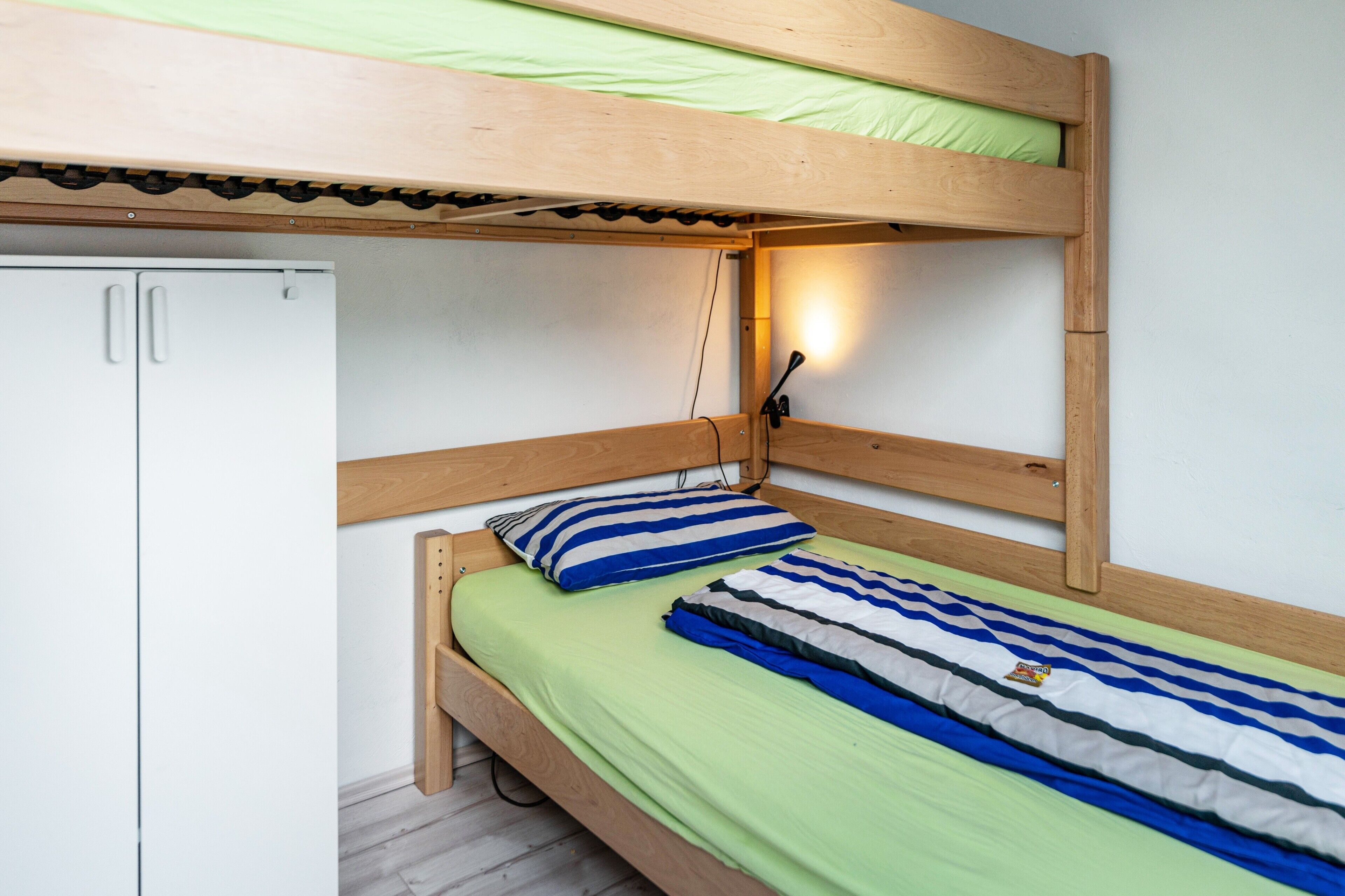 A bunk bed with a green mattress, striped pillows, and a wooden headboard.