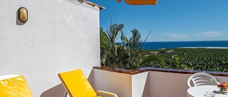 Una terraza con sillones amarillos, una mesa blanca con un florero y vista al océano.