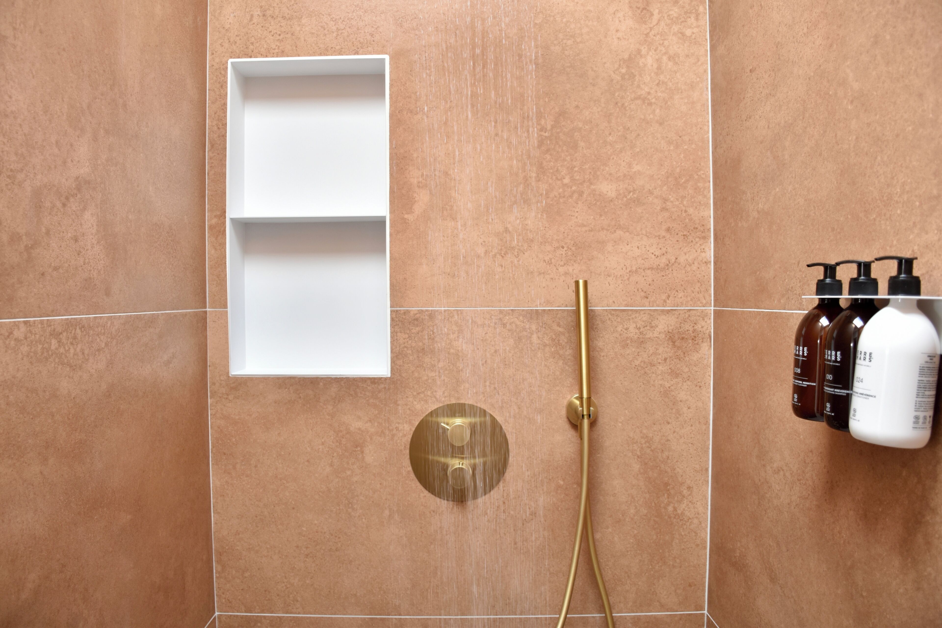 Un baño con ducha, un estante blanco y artículos de aseo.