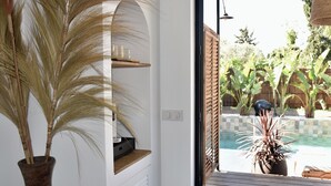 Et værelse med en stor potteplante, en hylde med kaffemaskine, og udsigt til swimmingpool og have.