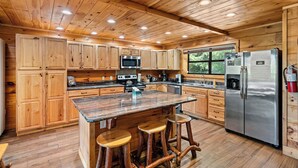 A spacious kitchen with wooden cabinets, a central island with stools, stainless steel appliances, and a large window providing natural light. - Private 2+ Acre Ridge-Top Retreat with Hot Tub, Game Room & Stunning Views! (Gatlinburg)