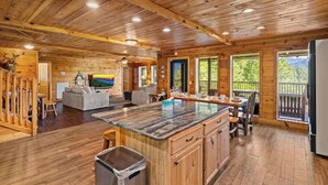 A spacious cabin interior with a large wooden dining area, a kitchen with a central island, and a living room with a sofa and television. - Private 2+ Acre Ridge-Top Retreat with Hot Tub, Game Room & Stunning Views! (Gatlinburg)