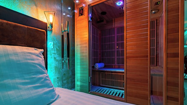 A room with a bed, a wooden sauna, and a wall-mounted heater.
