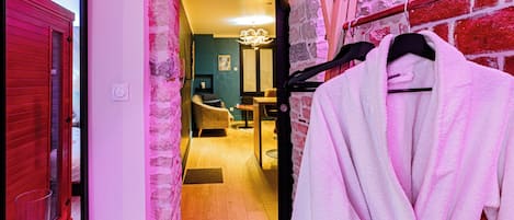 A hallway with a red door, a brick wall, and a robe hanging on a rack.