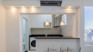 A modern kitchen with a built-in washing machine, pendant lights, and a view of the city through a window. - Complete Studio in Curitiba Eda0001 (Curitiba)