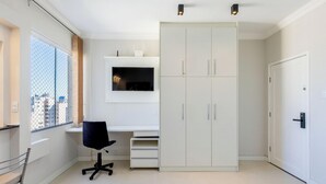 A modern bedroom with a large wardrobe, a desk with a chair, and a TV mounted on the wall. - Complete Studio in Curitiba Eda0001 (Curitiba)
