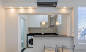 Una cocina moderna con lavadora integrada, luces colgantes y vistas de la ciudad a través de una ventana.